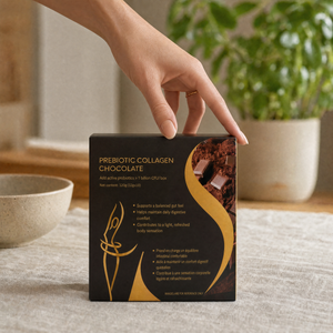 A hand placing a black and gold Nourrish prebiotic collagen chocolate box on a table beside a bowl and plant.